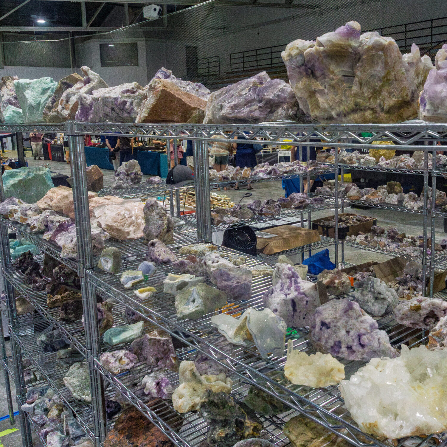 Large amethyst clusters and raw mineral formations on vendor shelving at the Kitchener Rock and Gem Expo